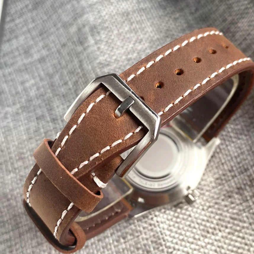 Brown leather watch strap with silver buckle on a gray textured background